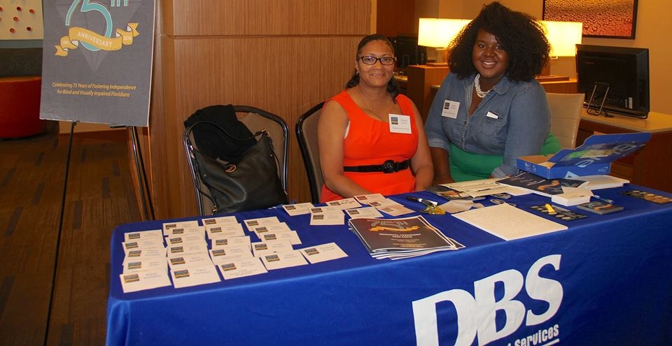 DBS staff members Cynthia Lyons and Kesha Royster sitting at the DBS welcome table during the 75th anniversary ceremony and expo.